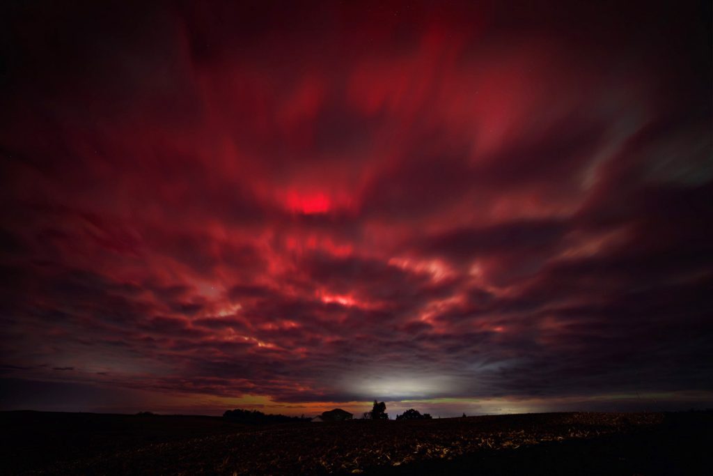 Photograph of red aurora shining through clouds: Timothy Hughes. timothyhughes.com.